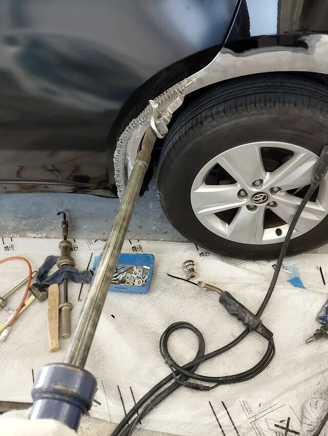 スライドハンマーで左クォーターの凹みを引き出す板金作業
