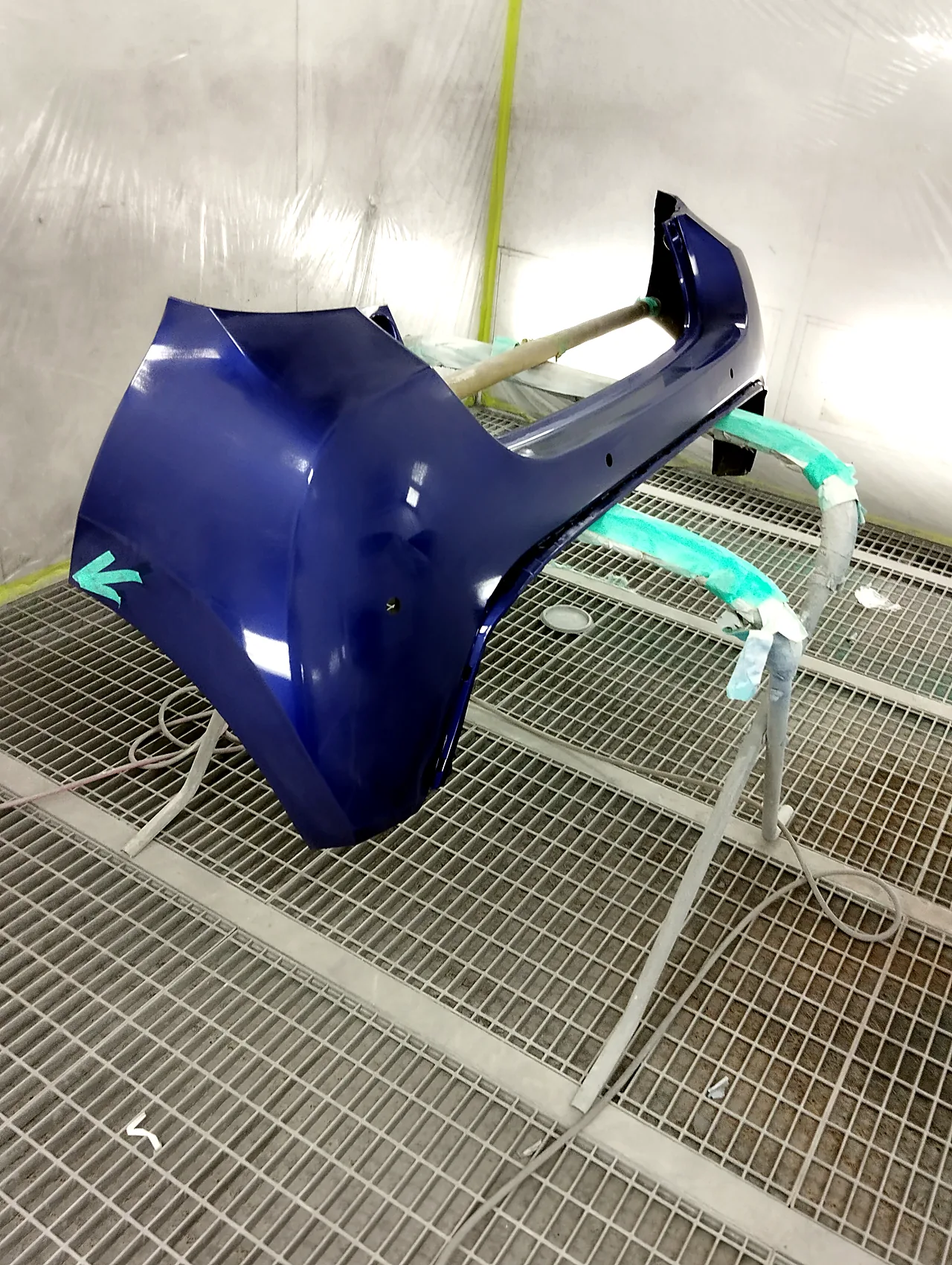 塗装ブースのスタンドに載せたヤリスのリヤバンパー(塗装前)。角に緑のテープの矢印