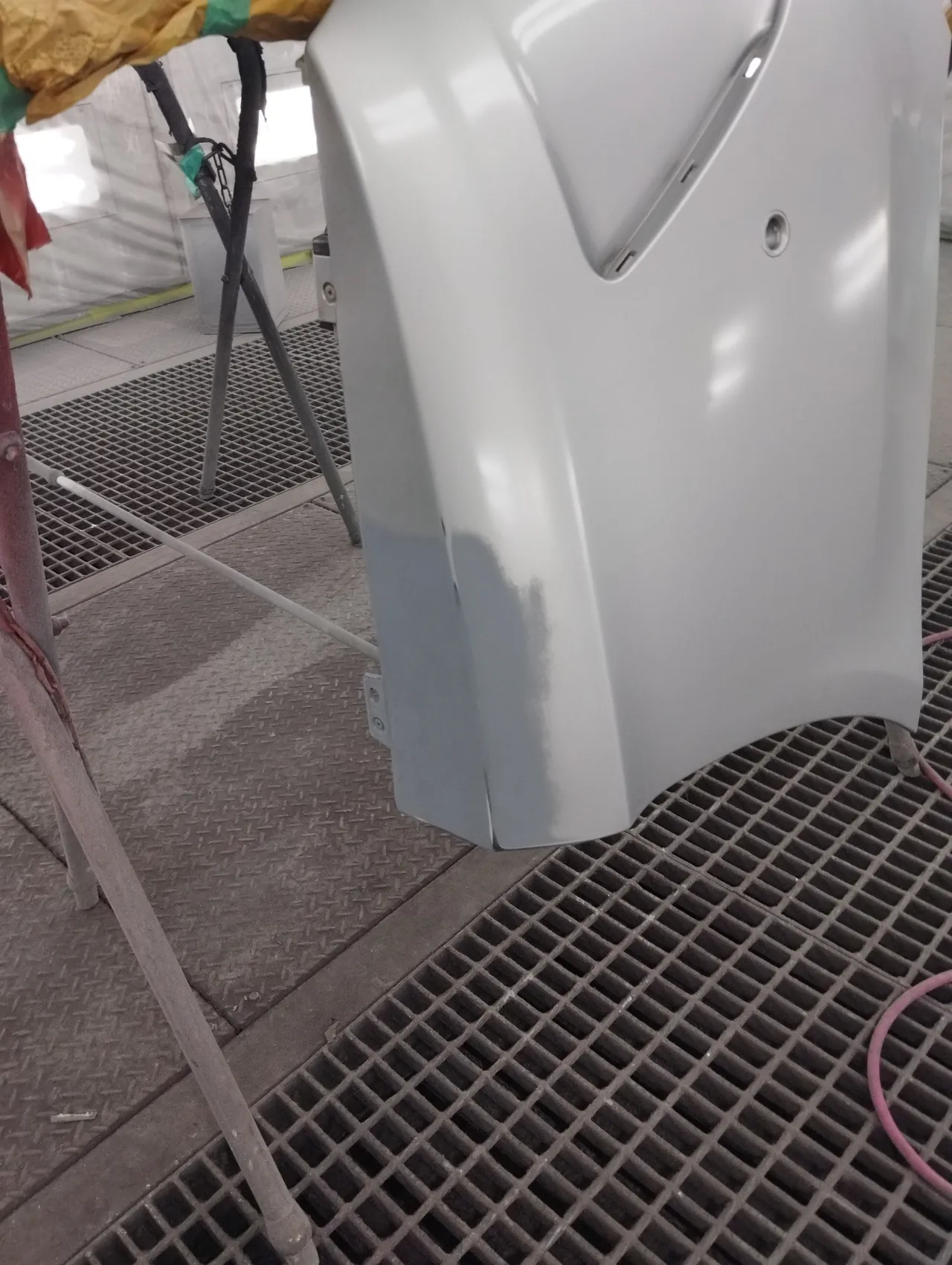 塗装ブースの台に載せた、塗る前のベンツCクラスのリヤバンパーの角。下の縁にサフェーサーの灰色