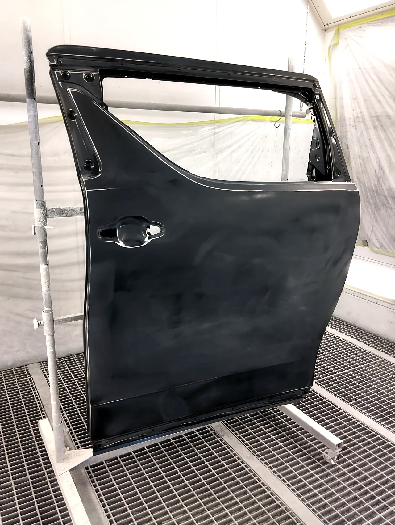 塗装ブースのスタンドに立てた30系アルファードの新品の左スライドドア。つやのない面に研いだ跡