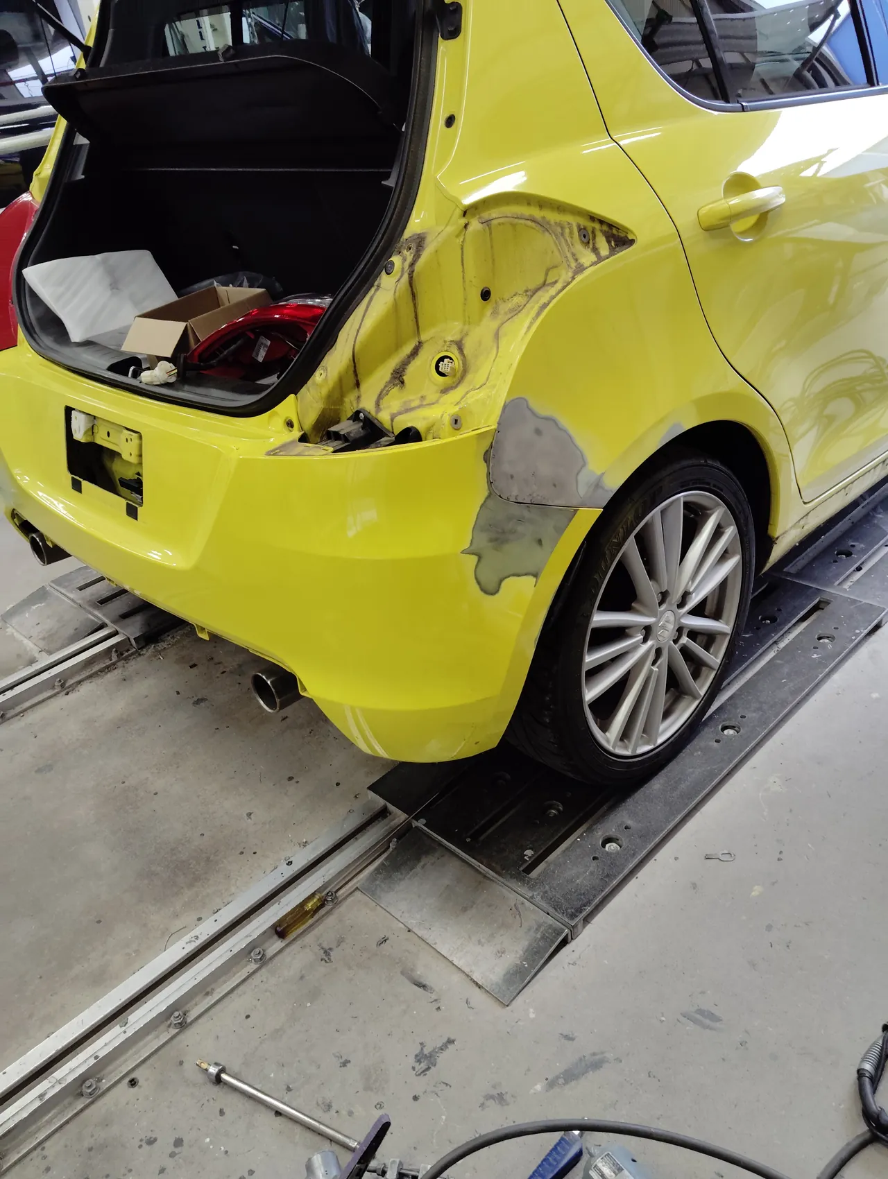 研いだリヤバンパーを一度車体に付けたスイフトスポーツの右後ろ。右テールランプは荷室に置いてあり、後ろのナンバーは外してある