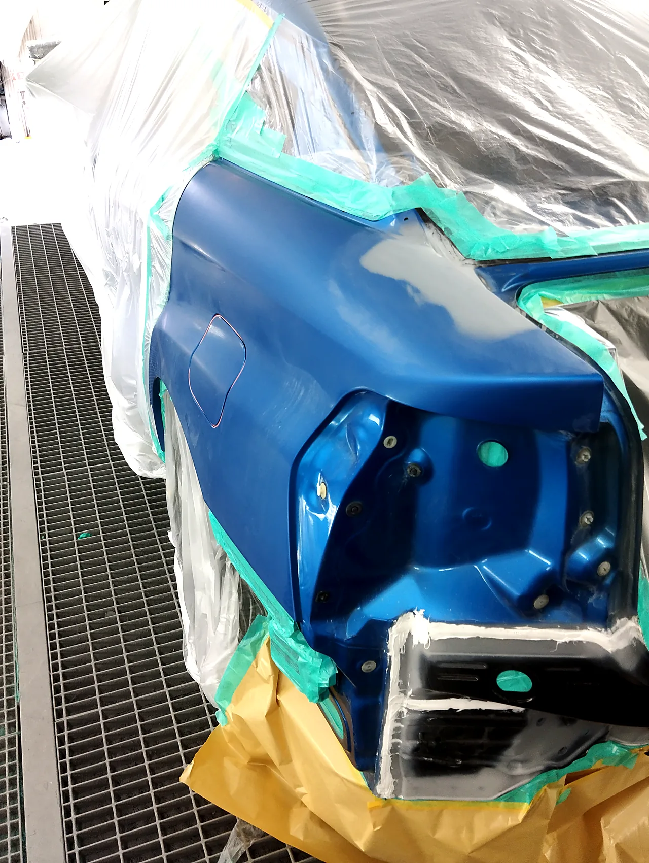 塗装ブースでマスキングしたMIRAIの左後ろの角。左リヤクォーターを出し、境に緑のテープ