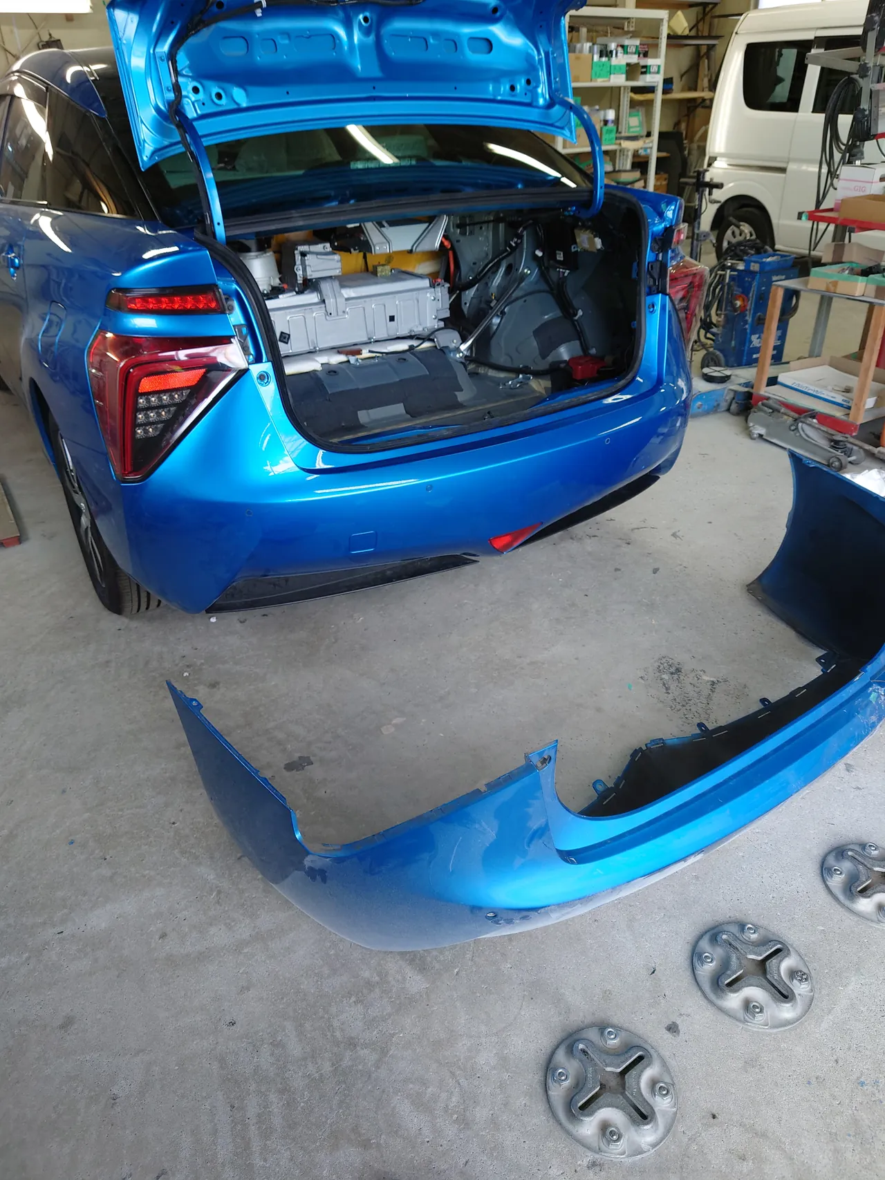 左後ろから見た組み付けの途中のMIRAI。塗装したトランクと新しいリヤバンパーが付き、床に外した元のリヤバンパー
