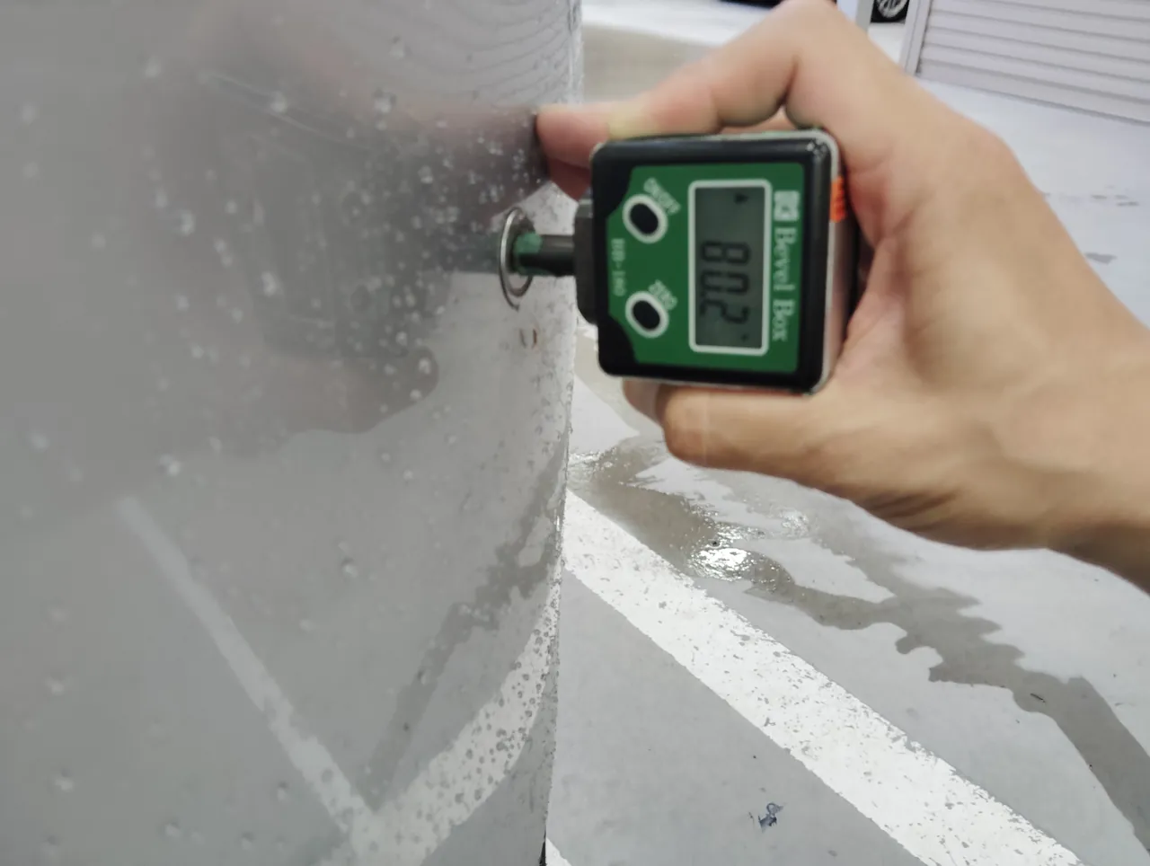 プリウスの車体の丸い部品にデジタル式の角度計の軸を当て、角度を表示しているところ(修理後)