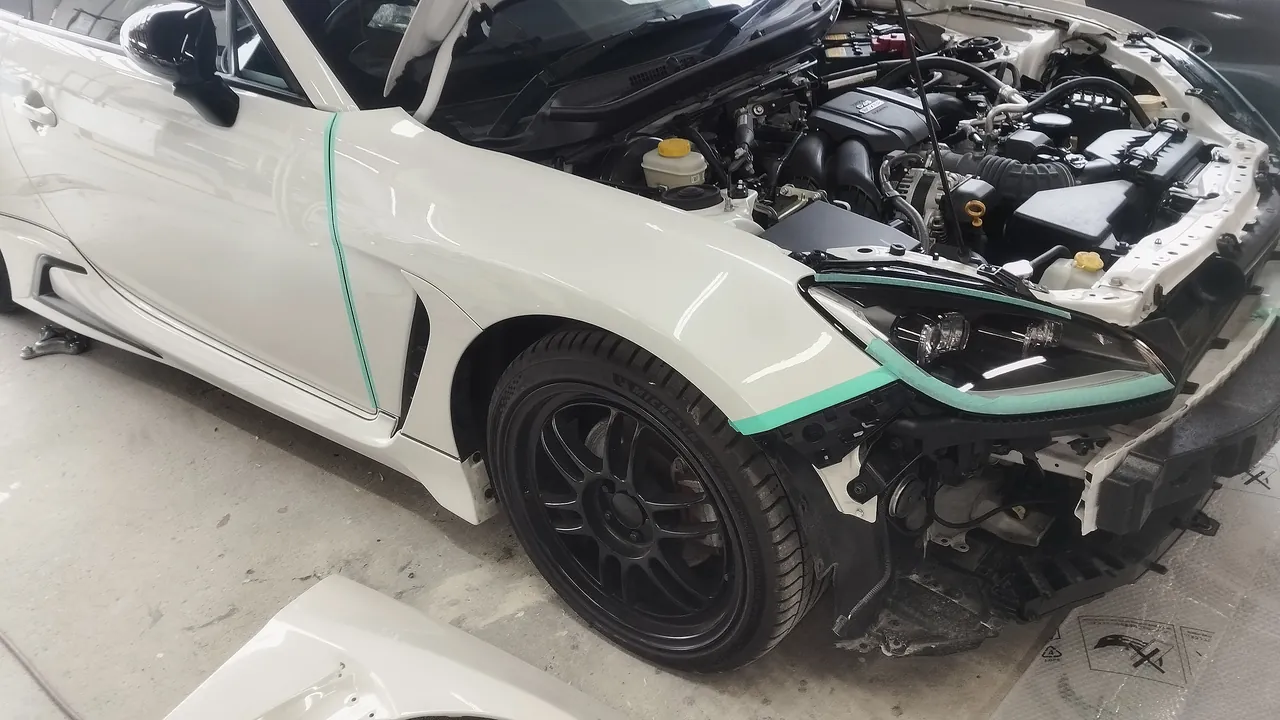 塗り終えた新品の右フロントフェンダーが付いたGR86（バンパーはまだ）。ヘッドライトの縁とドアとの境目に緑のテープ