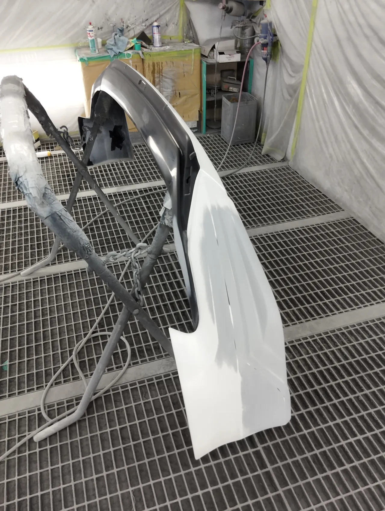 塗装ブースのスタンドに立てたカムリのフロントスポイラー右端。補修した範囲にグレーのサフェーサー(塗る前)