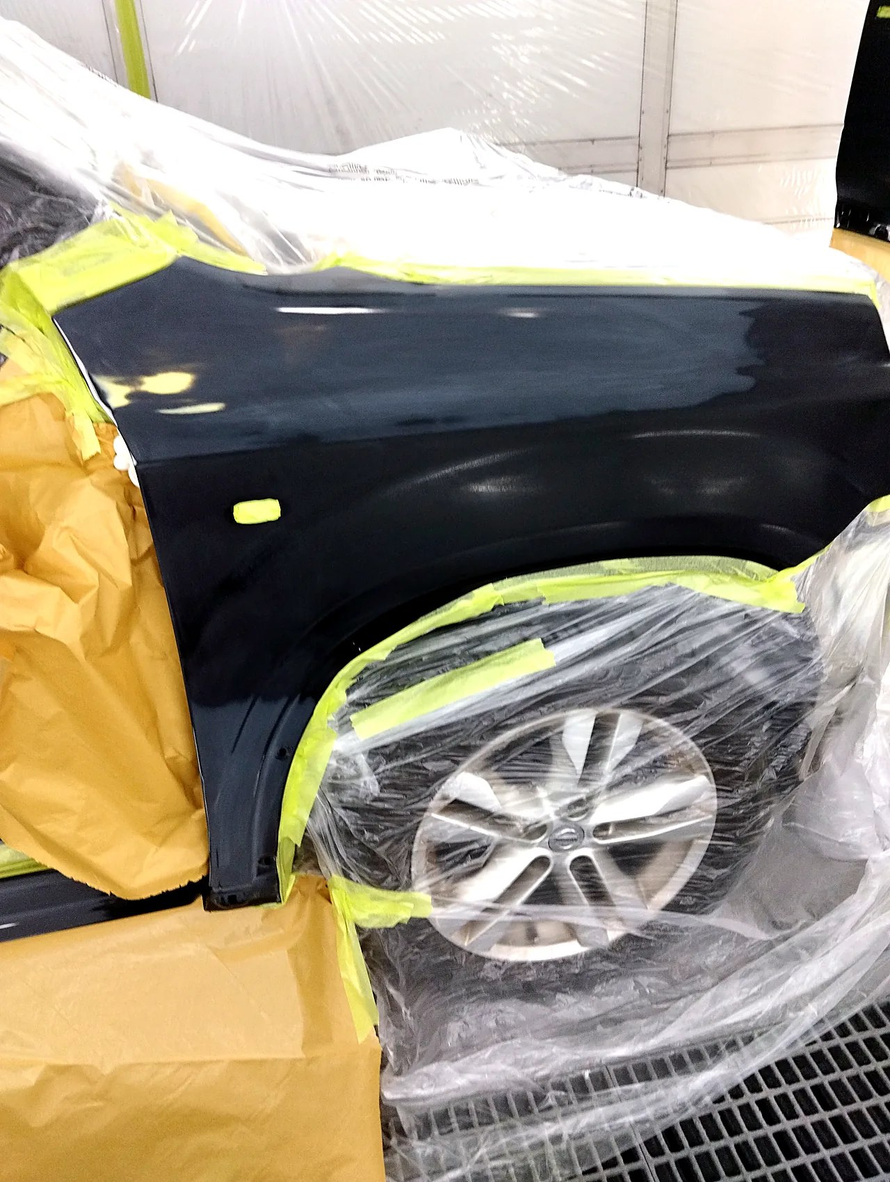 塗装ブースで塗る前の日産 T31エクストレイルの右フロントフェンダー。車体はフィルムで包み、横の小さな穴にテープ