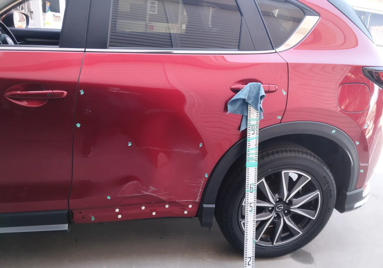 修理前のマツダ CX-5の左リヤドア。後輪のそばに目盛りの棒を立てて、へこみの高さを記録