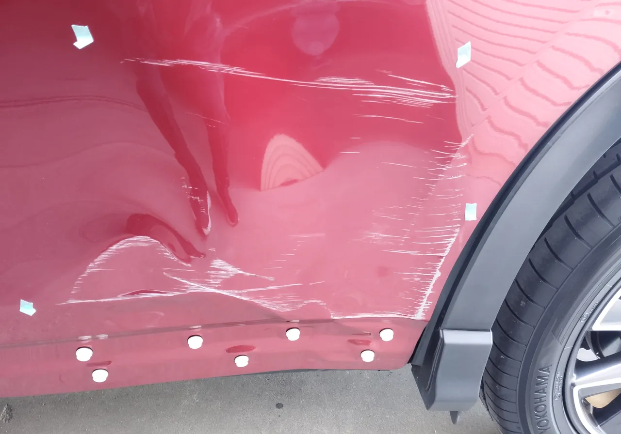 修理前のマツダ CX-5の左リヤドアの寄り。波打つような深いへこみと横向きの擦り傷、ドア下の白い丸い留め具