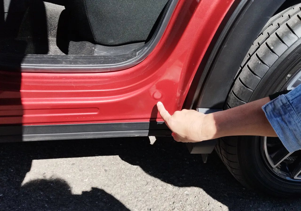 マツダ CX-5の左リヤドアを開けた開口部の下の角（サイドシルの後ろの端）を指でさしたところ（修理前）