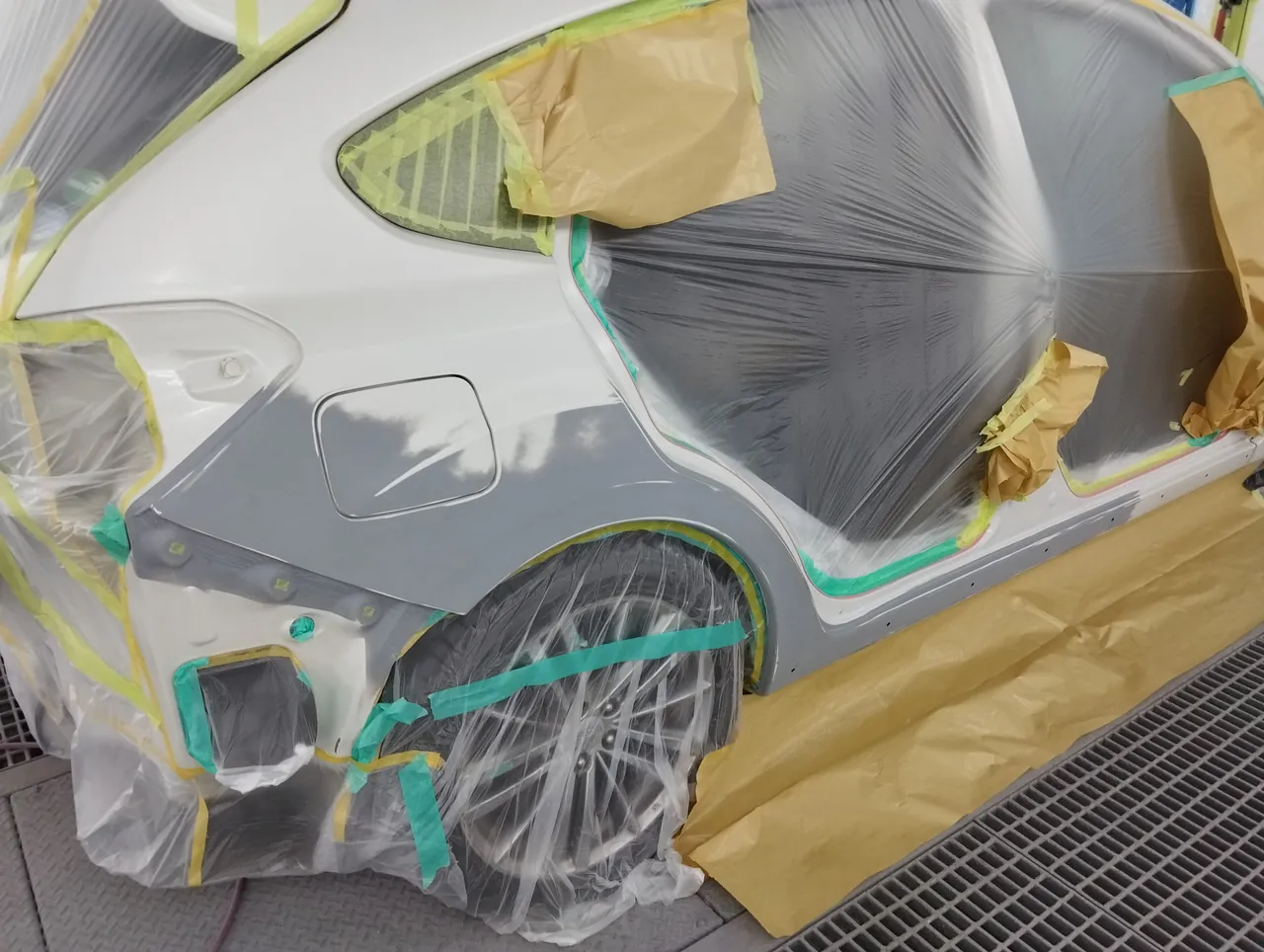 塗装ブースのインプレッサ。右リヤクォーターの下に灰色のサフェーサー、ドアの開口部はビニールで覆う