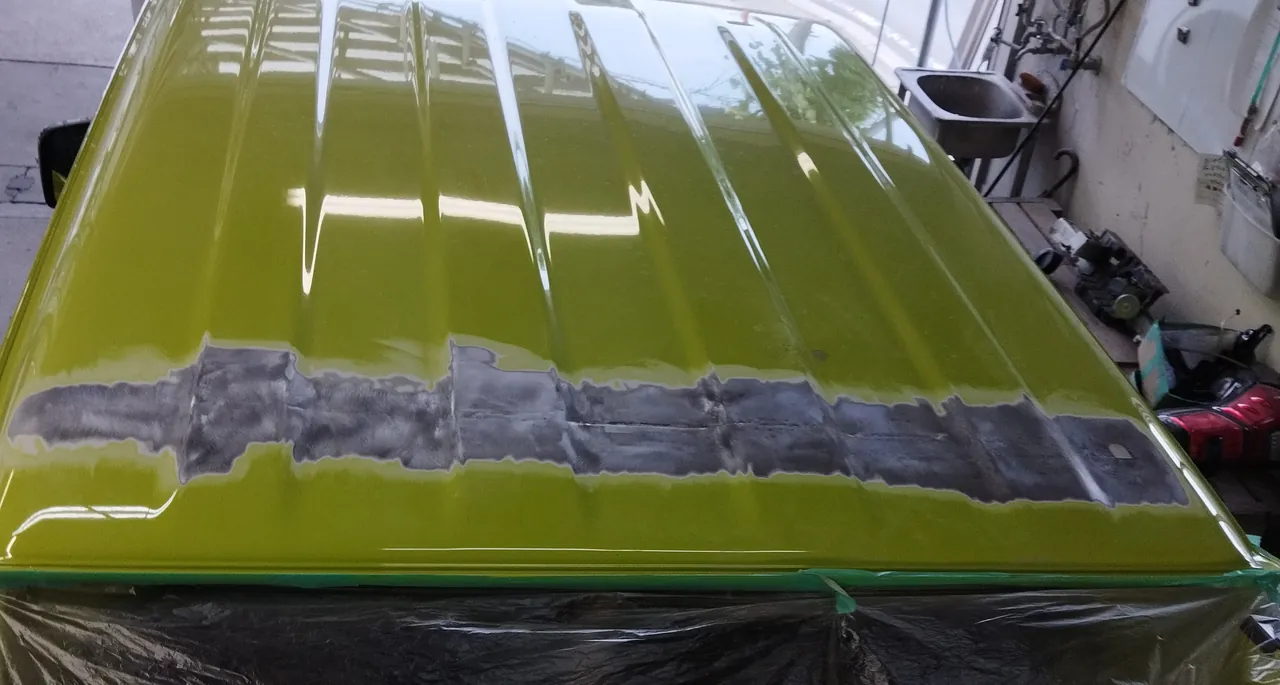 研いで鉄板を出した帯が屋根の幅いっぱいに走るジムニー（JB64）を後ろから。車体はビニールで覆う