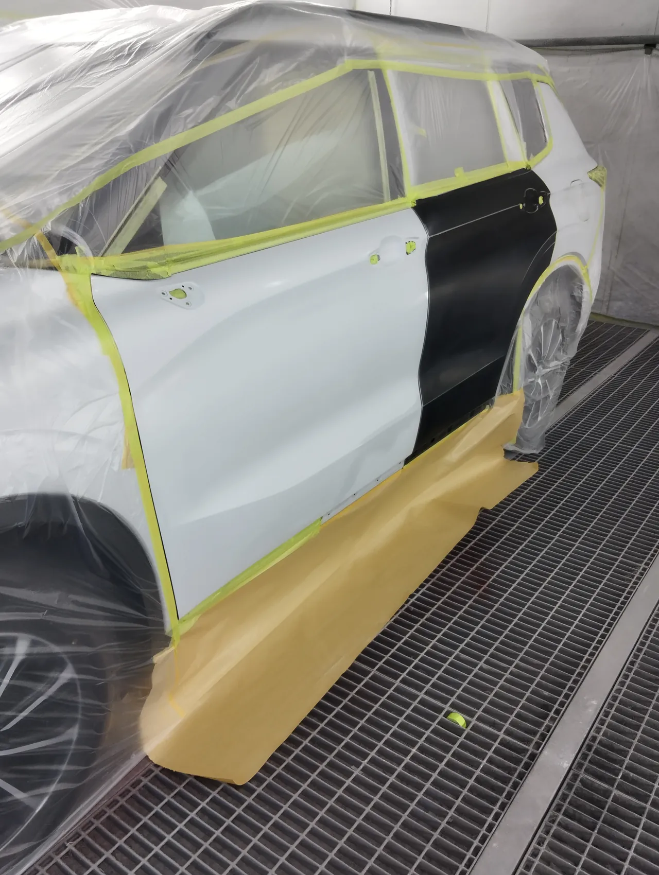塗装ブースでビニールに包んだアウトランダーPHEV。左前ドア・黒い新しい左リヤドア・左リヤクォーターを出し、ドアミラーと取っ手は外して穴をテープでふさぐ