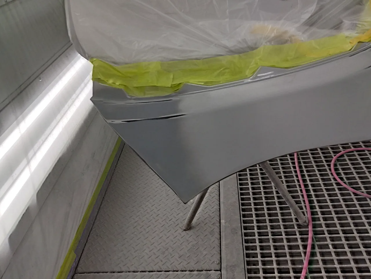 台に載せたシエンタのリヤバンパー。上側をビニールで覆い、プレスラインに沿ってテープで区切る(塗る前)