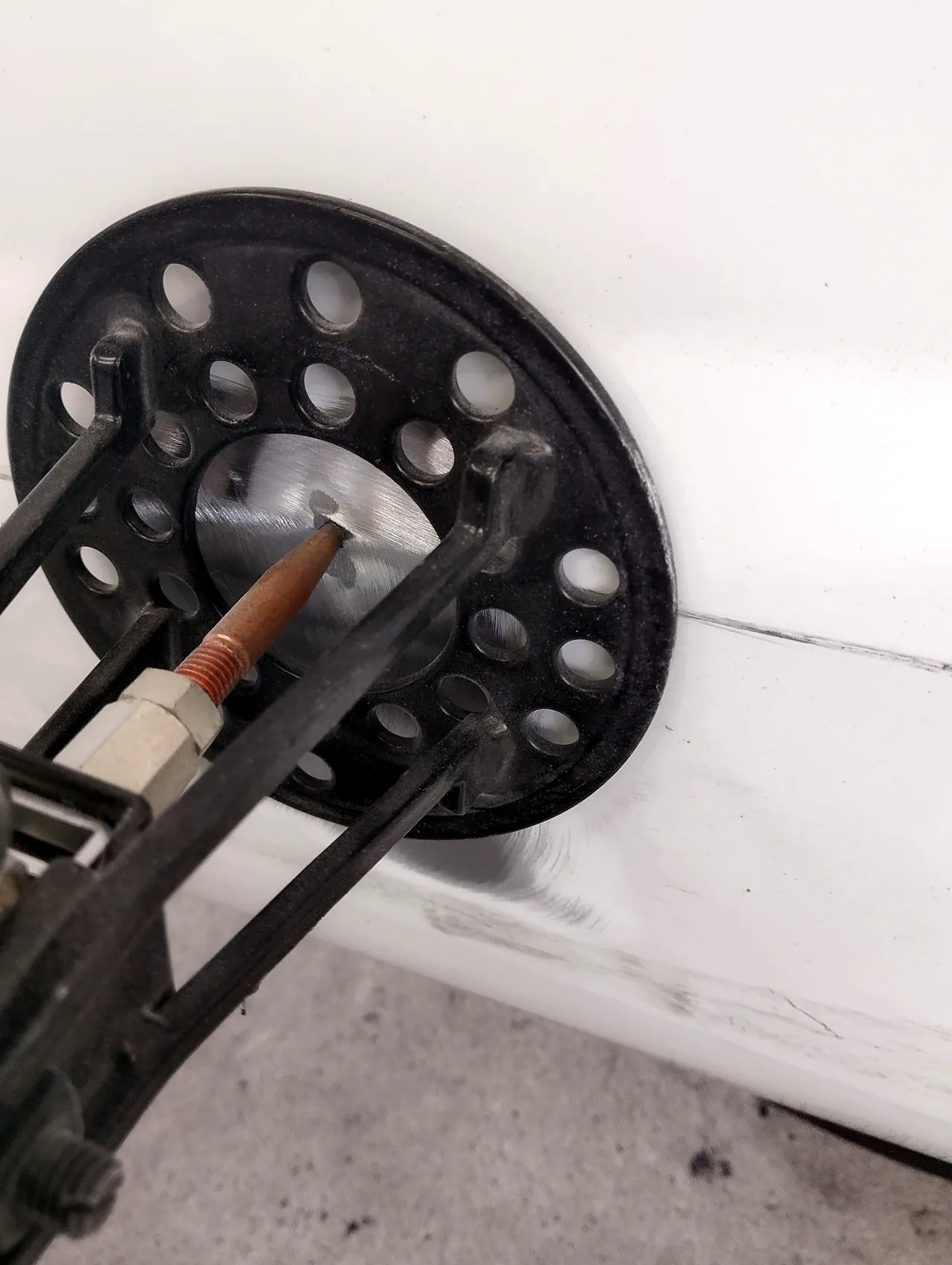 エブリイの右スライドドア。研いだ鉄板に、レバー式の工具の先の銅色のピンを当て、丸い穴のあいた当て板でまわりを押さえて引く