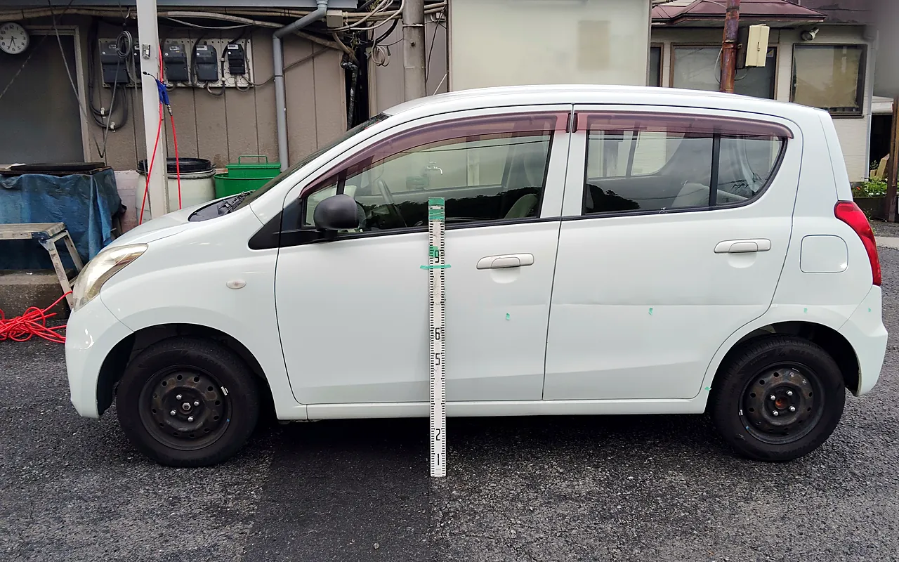 修理前のスズキ アルト エコを左真横から。前ドアからリヤバンパーの角まで緑のテープの印が並び、目盛りの棒を立てて記録