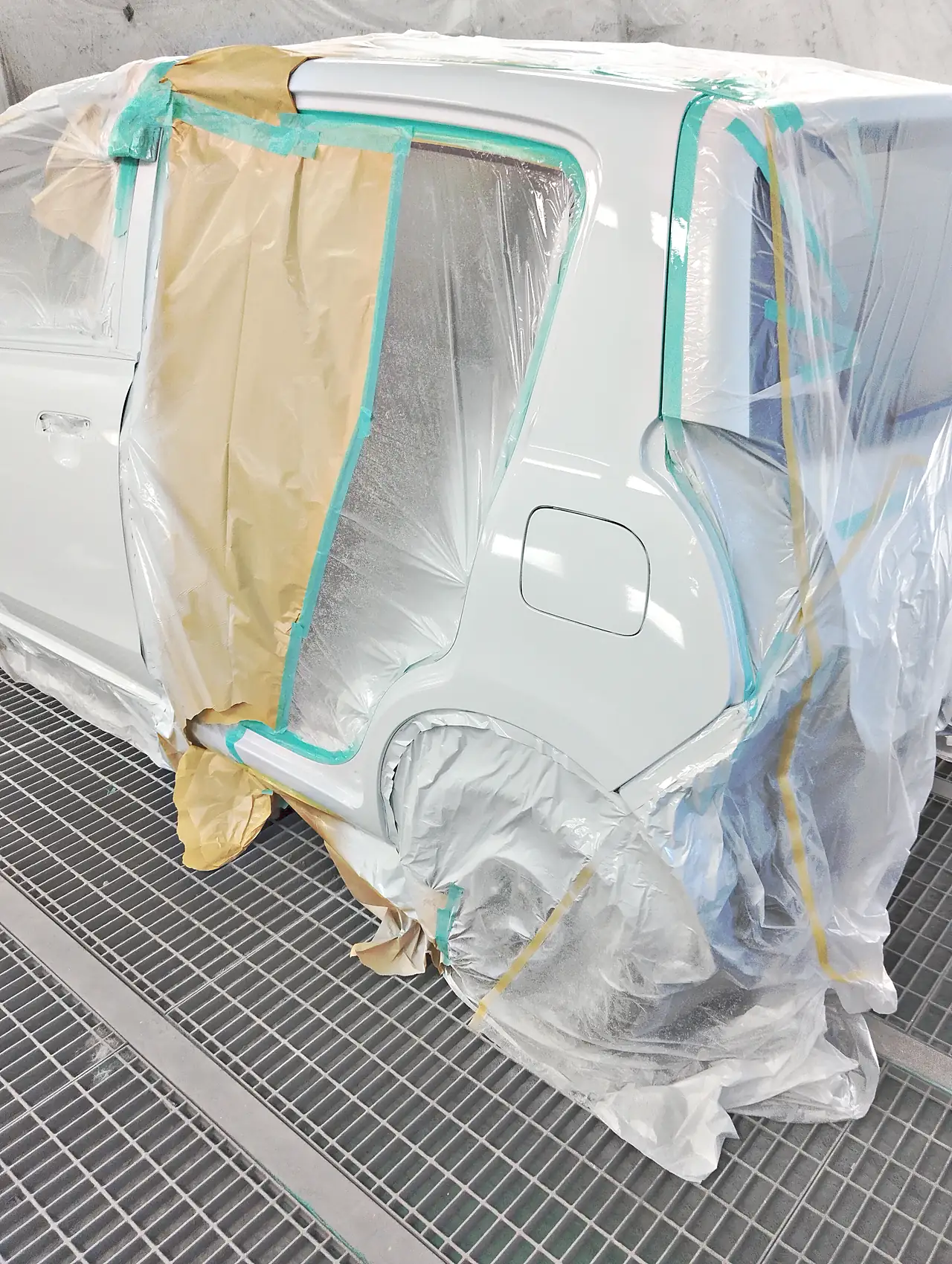塗装ブースで、カラー番号ZUDの白に塗り終えたアルト エコの左リヤクォーター。つやのある面に照明が映り込む