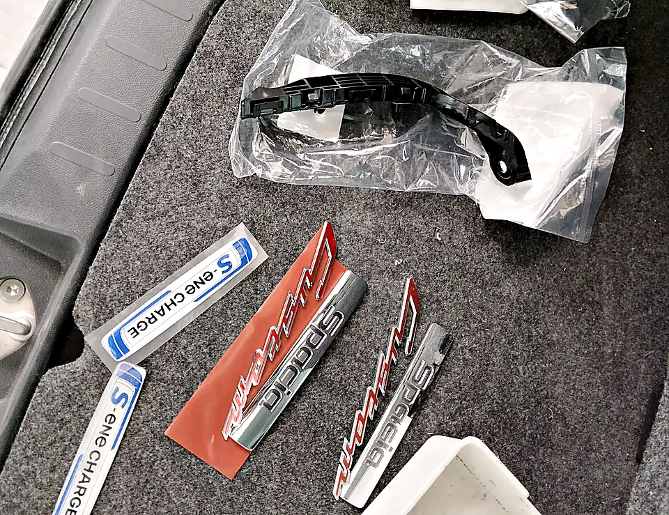 スペーシア カスタムに付ける新しいエンブレム2つ(Spacia Custom・S-ene CHARGE)と、外した元のエンブレム、袋に入った新しい取付け部品