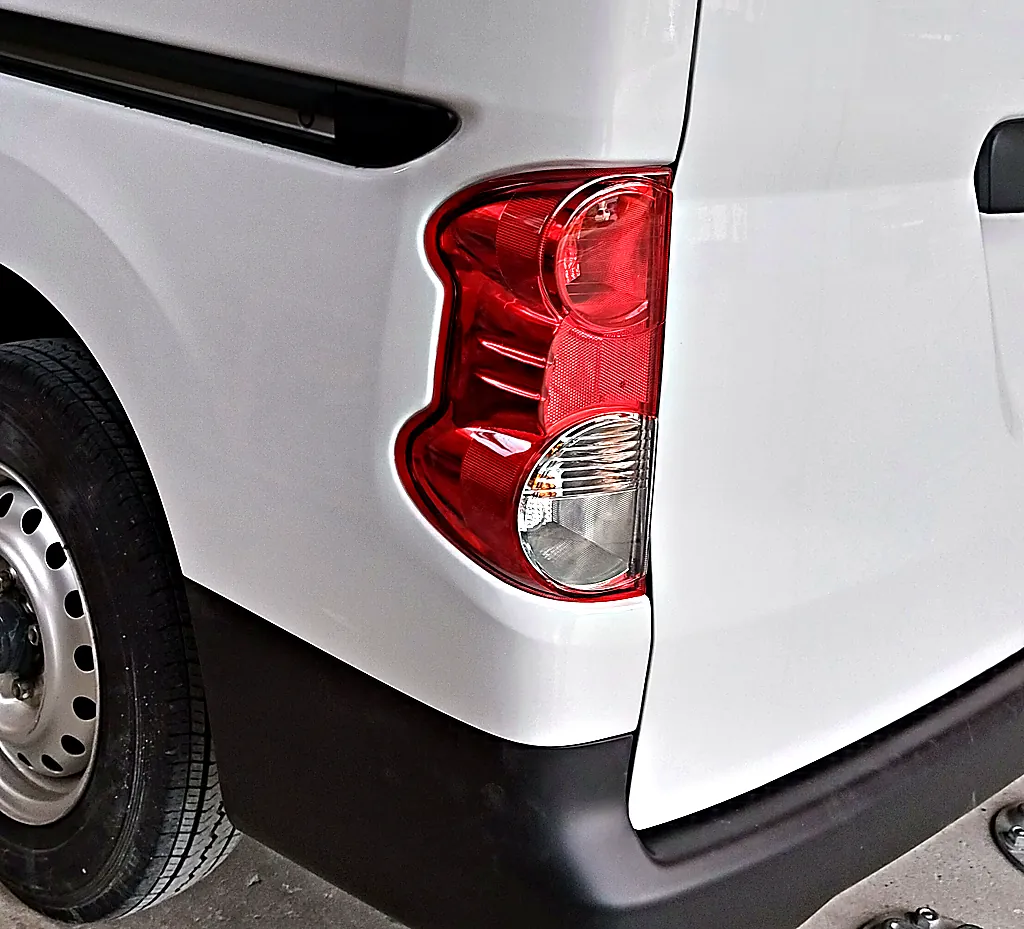 修理後のNV200バネット バンの左後ろの角。新しい左テールランプとリヤバンパー、塗り直した左リヤクォーター（工場の中）