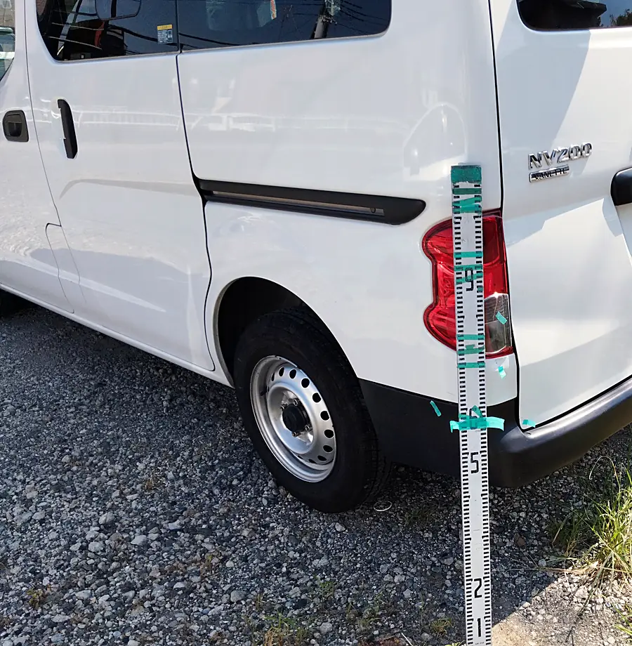 NV200バネット バンの左後ろの角に目盛りの付いた棒を立て、傷の高さを記録した写真（修理前）