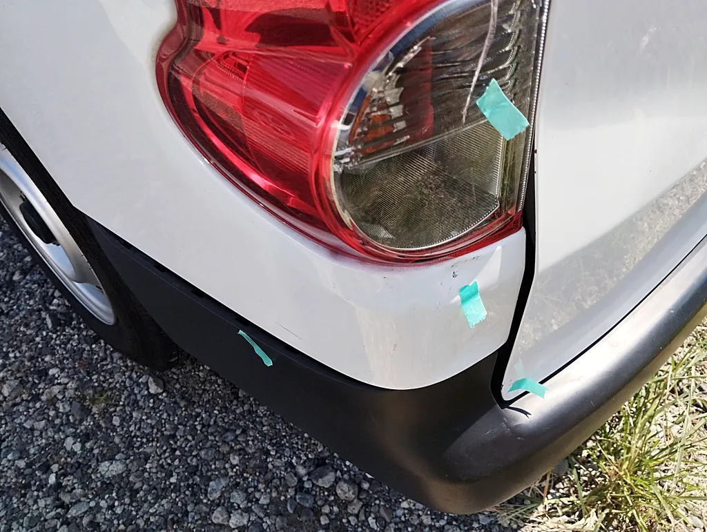 NV200バネット バンの左テールランプの下の角。白い角がへこみ、黒い擦れと緑のテープの印（修理前）