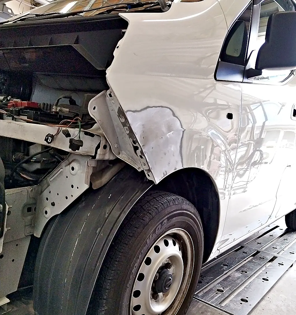 前バンパーと左ヘッドランプを外したNV200バネット バンの左フロントフェンダー。下の前の角を研ぎ、鉄板が出ている