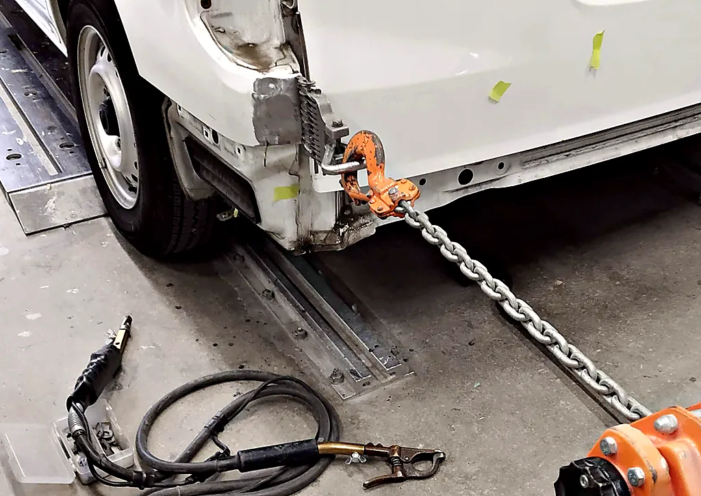 NV200バネット バンの左後ろの角の下の縁にクランプを掛け、チェーンで後ろへ引いているところ（寄り）
