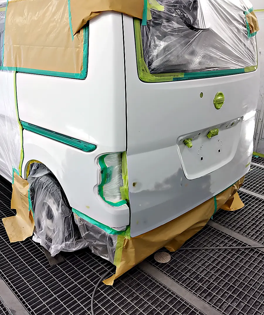塗装ブースのNV200バネット バンの後ろ。取っ手とバッジを外したバックドアと左リヤクォーター、テープで覆ったNISSANのエンブレム（塗装前）